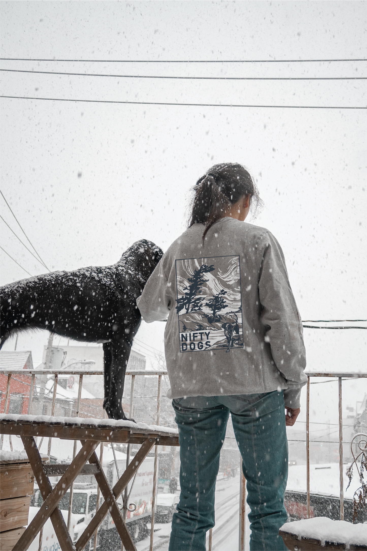 Back of Nifty Dogs grey crewneck worn on person beside dog in snow